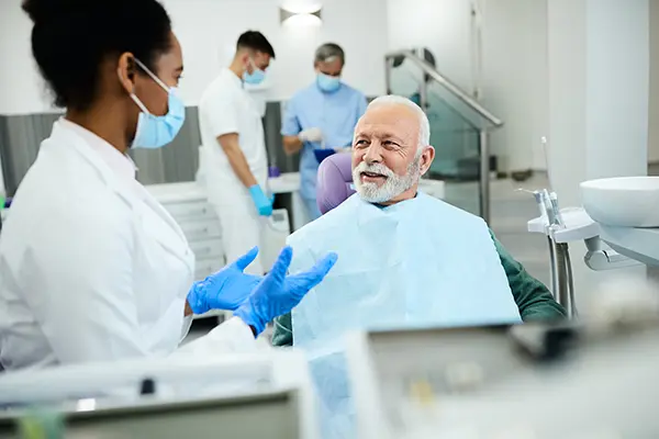Older white patient sitting in dental chair calmly discussing his oral health with his Black female dentist