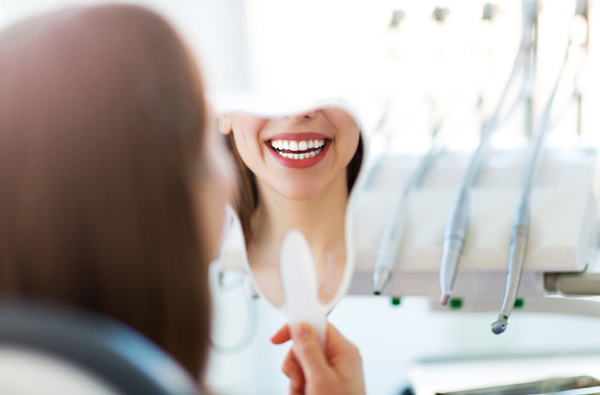 Woman looking at her smile in a mirror, at Meadowlark Dental in Salem, OR.